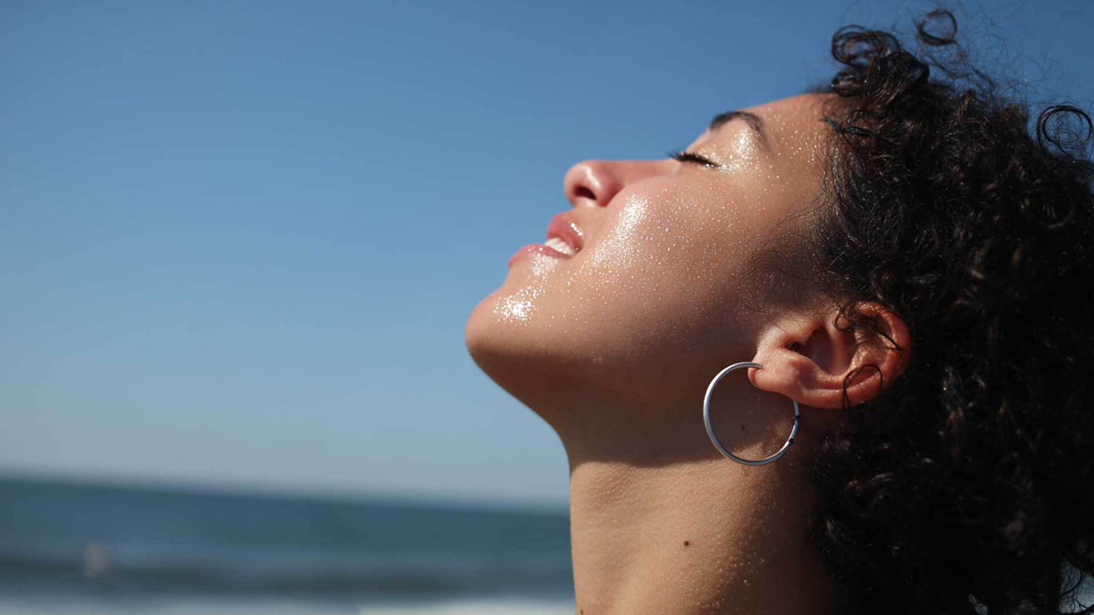 A woman tilting her face towards the sun against a clear sky