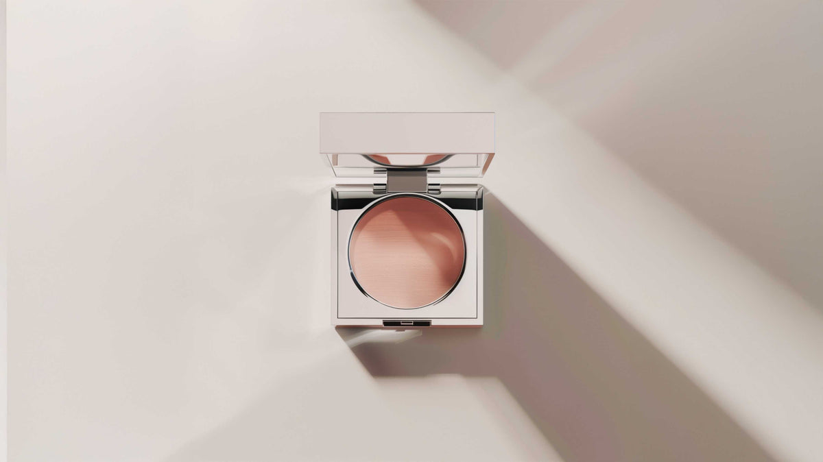 An open compact of beige cream lit from the side