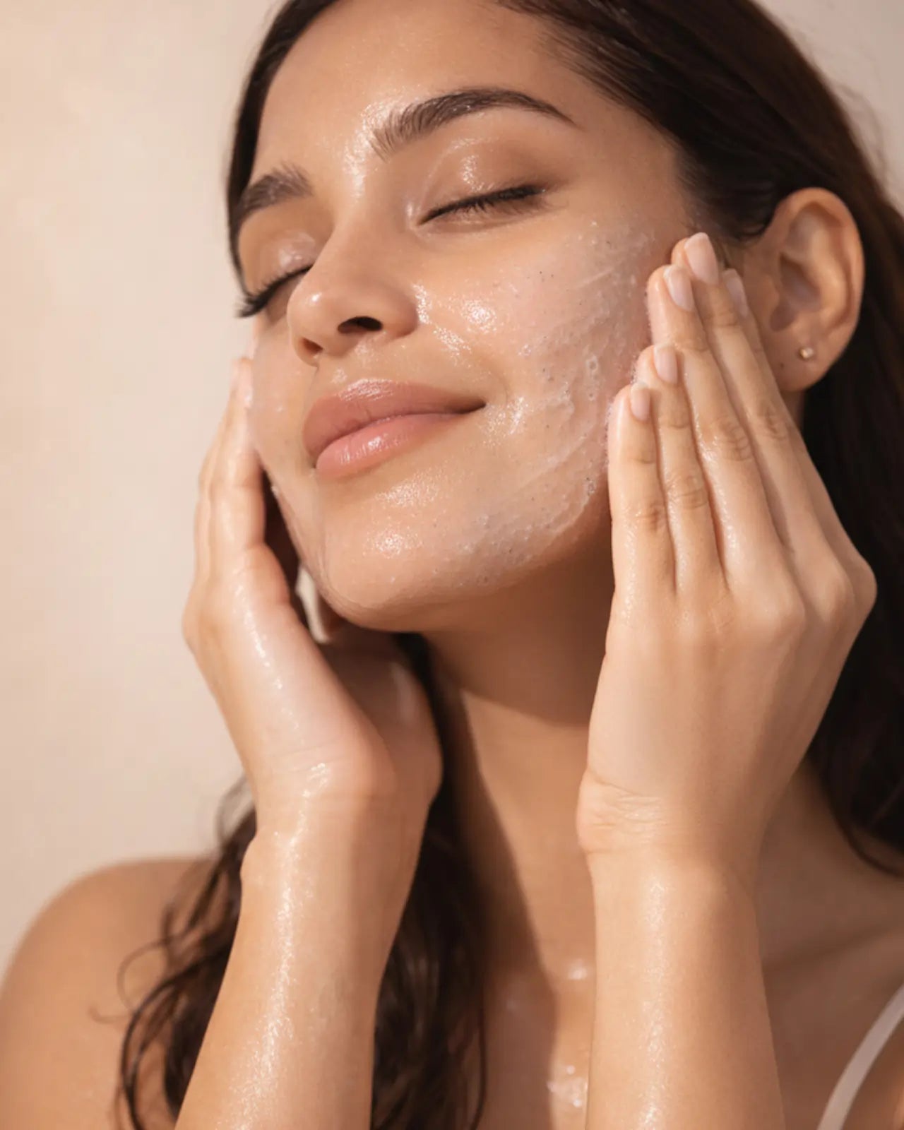 A woman rinsing a pale product from her face with both hands