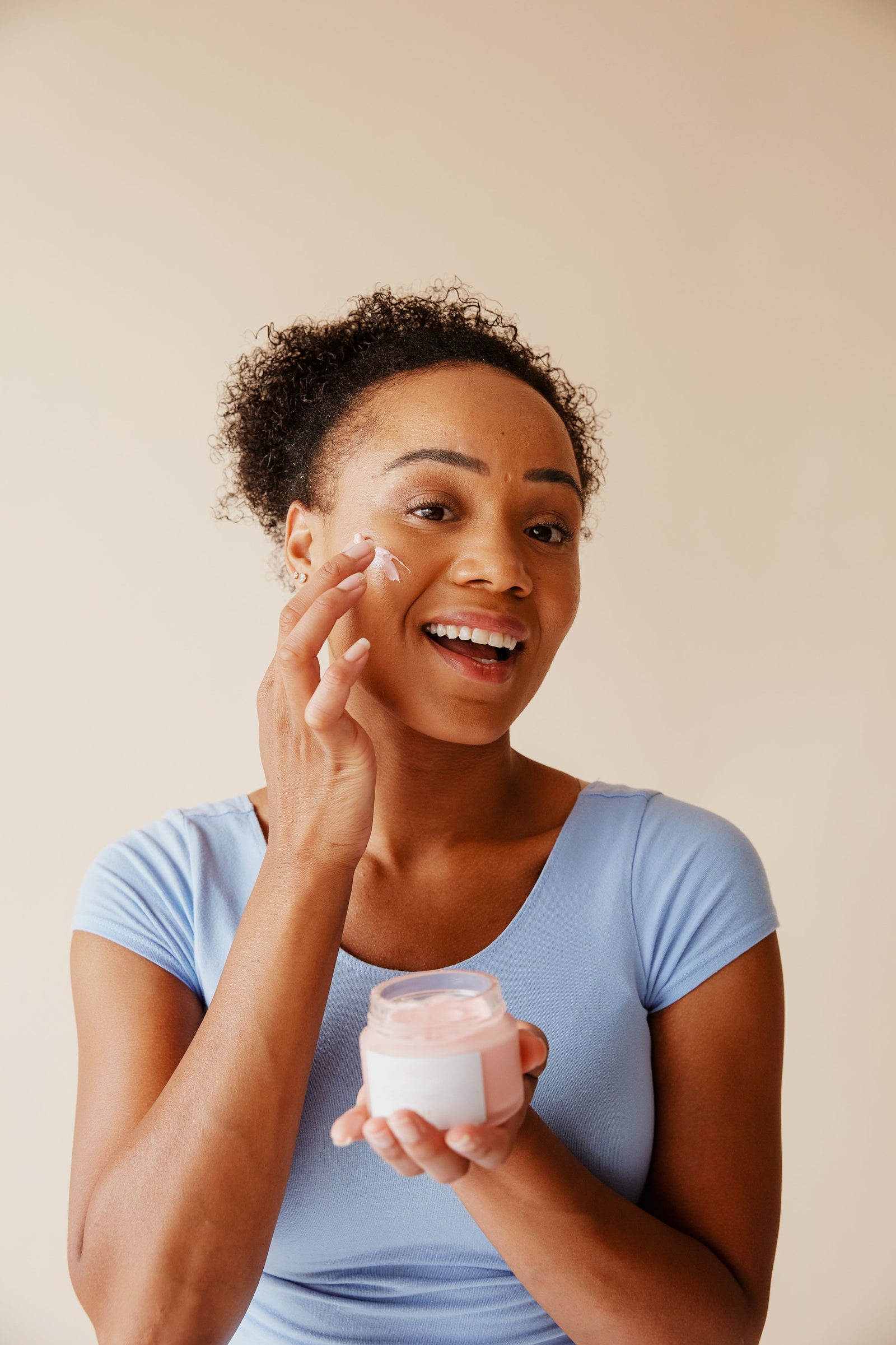 A woman applying cream from an open jar to her cheek